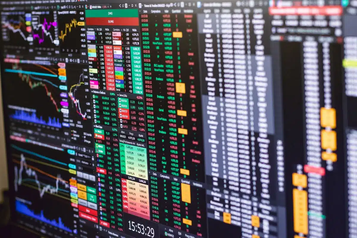 Investitori osservano grafici finanziari e dati di mercato su schermi luminosi in una sala trading moderna.