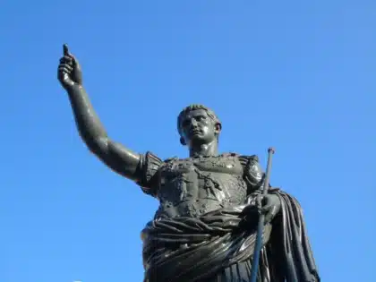 Opere metalliche lucide fra resti archeologici con visitatori in silhouette