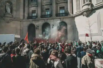 Folla anonima in piazza con mani alzate davanti a edifici pubblici sfocati