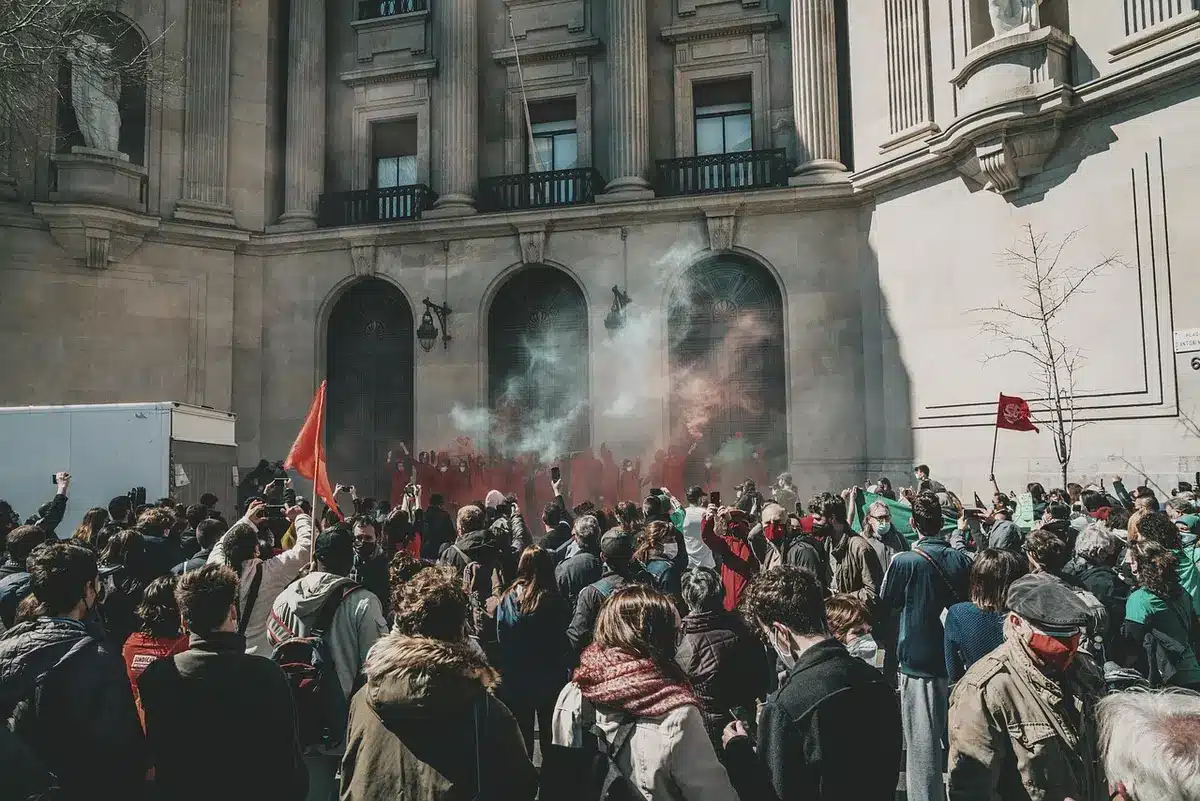 Folla anonima in piazza con mani alzate davanti a edifici pubblici sfocati