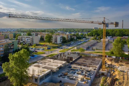 Cantieri e gru al tramonto con planimetrie su un tavolo, figure anonime sullo sfondo